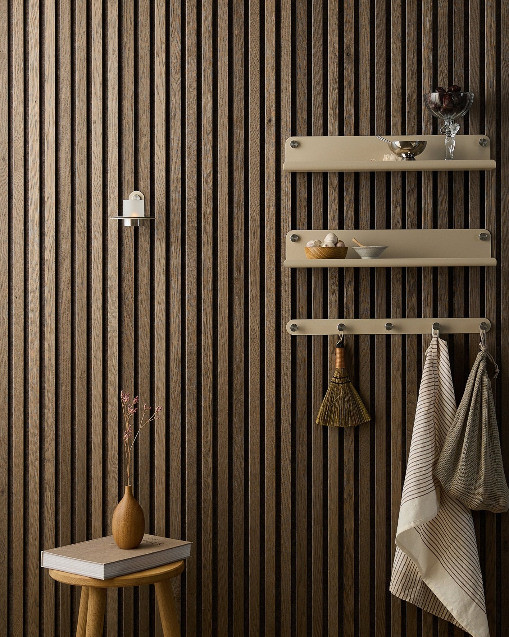 Drewniany stołek z suszonymi kwiatami stoi obok Akupanel Panel akustyczny od WoodUpp, obok półek beige z naczyniami, szczotką, ręcznikami i świecznikiem Norr.